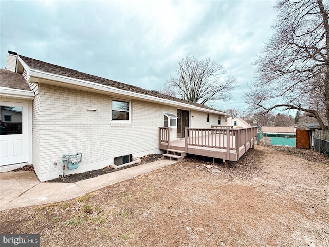 rear view of house with a deck, brick siding, a shingled roof, and fence