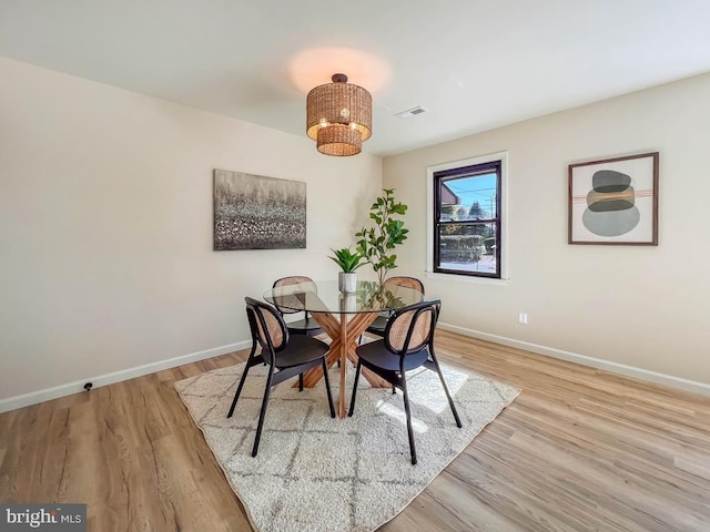 dining area with light wood-type flooring, baseboards, and a notable chandelier