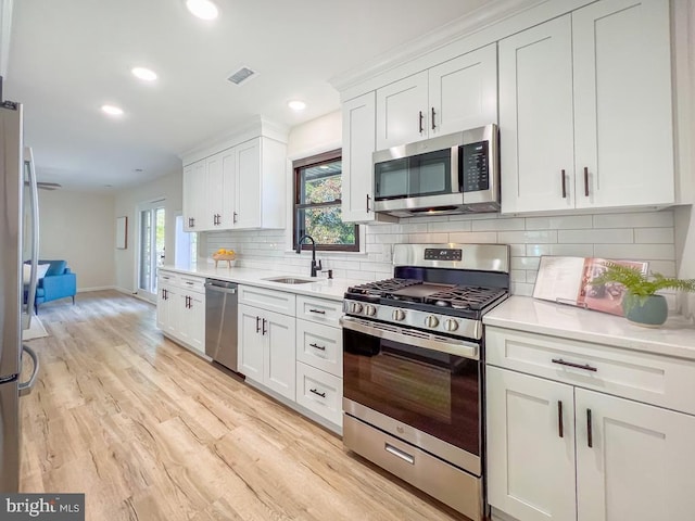 kitchen featuring stainless steel appliances, a sink, visible vents, light wood-style floors, and light countertops