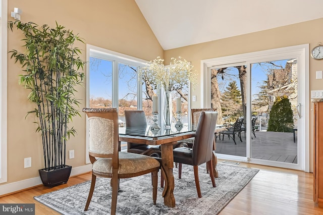 dining room featuring lofted ceiling, light wood-style flooring, baseboards, and a wealth of natural light