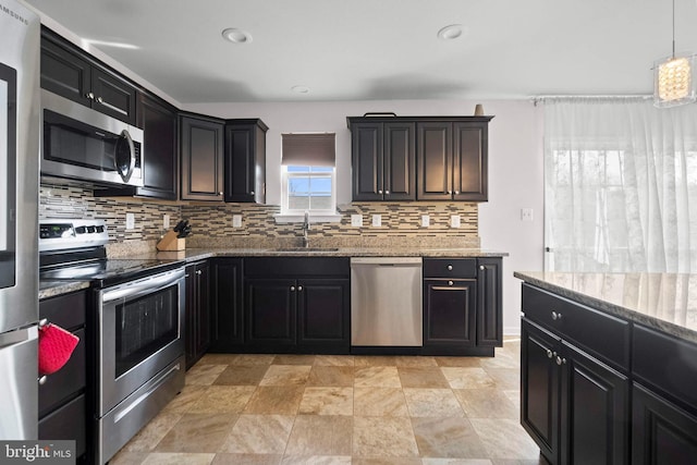 kitchen featuring a sink, backsplash, dark cabinetry, stainless steel appliances, and light stone countertops