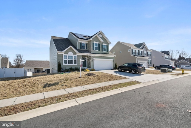 traditional home with fence, driveway, an attached garage, a residential view, and roof mounted solar panels