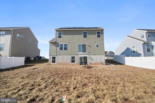 back of property with roof mounted solar panels, central AC, and fence