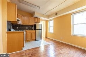 kitchen featuring backsplash, light wood-type flooring, freestanding refrigerator, and baseboards