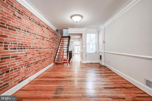 hallway featuring crown molding, visible vents, brick wall, wood finished floors, and baseboards