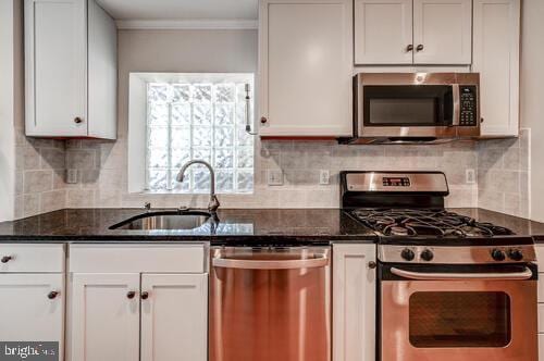 kitchen featuring stainless steel appliances, dark stone countertops, a sink, and white cabinets