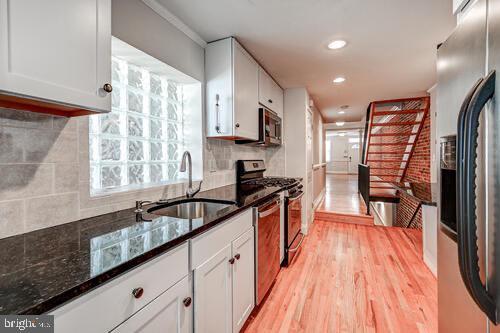 kitchen with light wood-style flooring, stainless steel appliances, a sink, white cabinetry, and backsplash