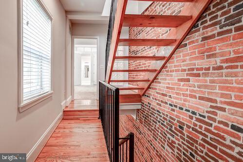 stairs featuring baseboards, brick wall, and wood finished floors