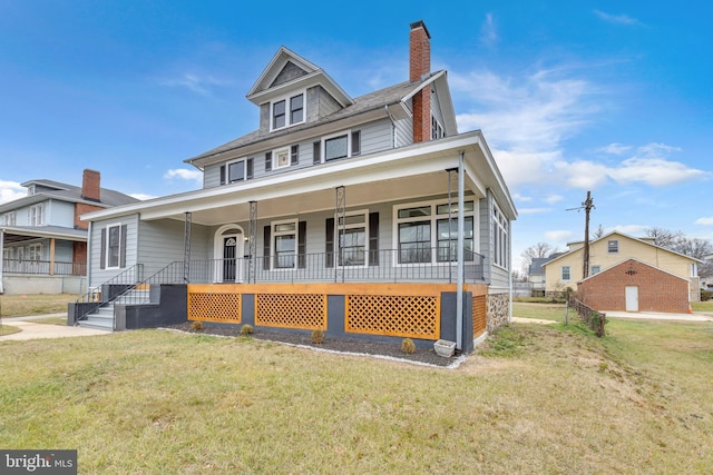 american foursquare style home with covered porch, a front lawn, and a chimney