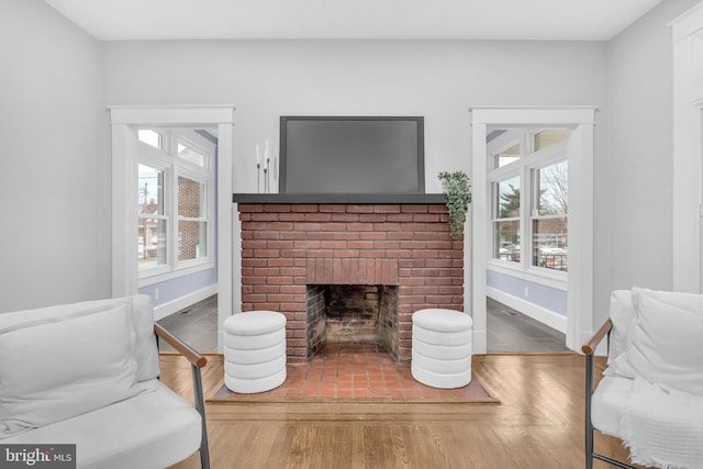 sitting room featuring a brick fireplace, baseboards, and wood finished floors