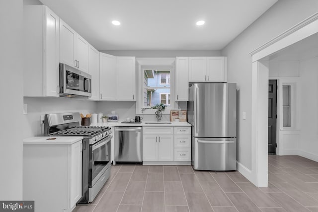 kitchen with white cabinets, stainless steel appliances, light countertops, a sink, and recessed lighting