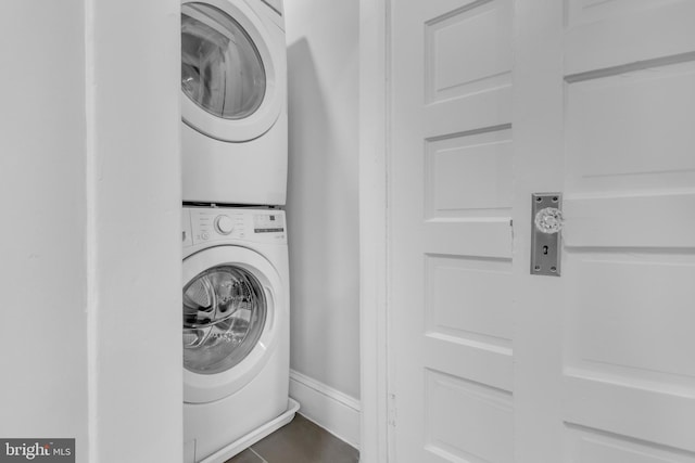 clothes washing area featuring laundry area, tile patterned flooring, baseboards, and stacked washer and clothes dryer