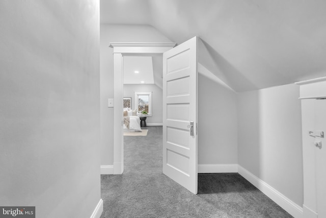 hallway with carpet floors, baseboards, and vaulted ceiling