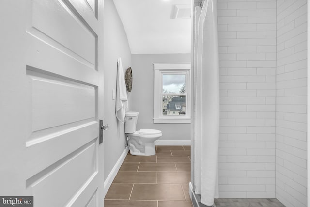 bathroom featuring toilet, tile patterned flooring, baseboards, and a tile shower