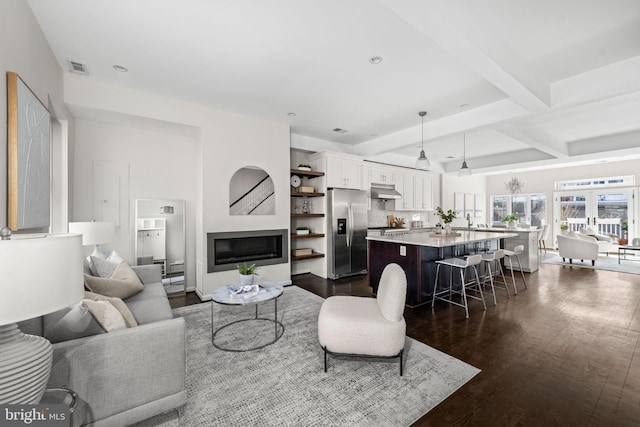 living area featuring visible vents, a glass covered fireplace, dark wood-type flooring, beam ceiling, and recessed lighting