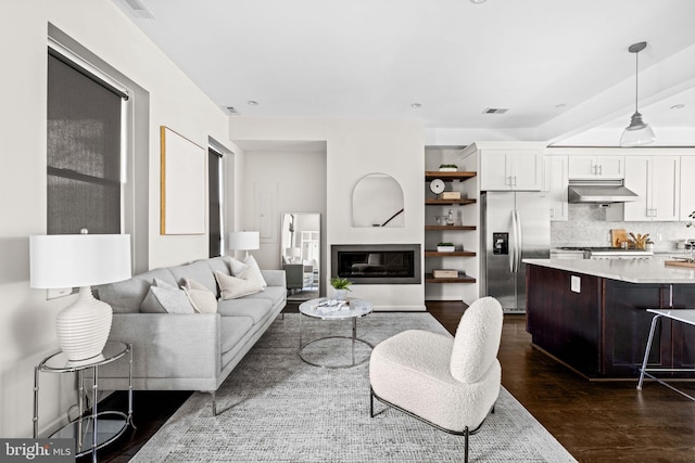 living area featuring dark wood-style floors, a glass covered fireplace, and visible vents