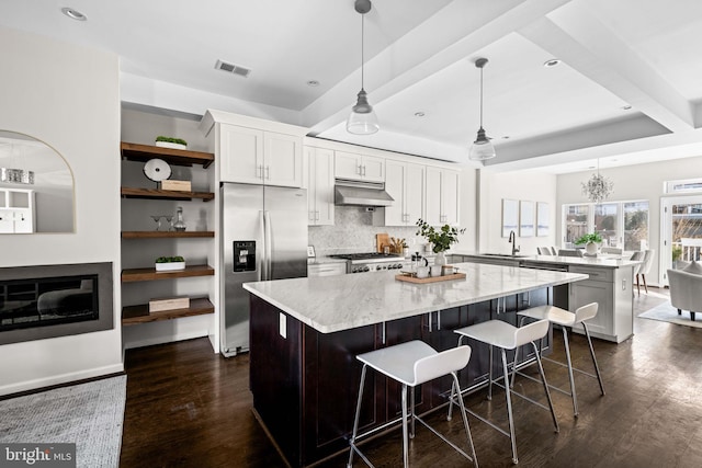 kitchen with stainless steel fridge, visible vents, a peninsula, under cabinet range hood, and a sink