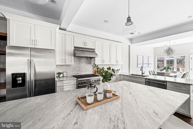 kitchen featuring light stone counters, appliances with stainless steel finishes, a sink, a peninsula, and under cabinet range hood