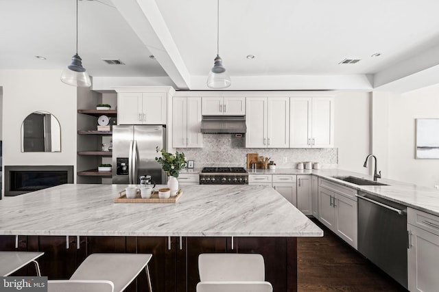 kitchen with tasteful backsplash, appliances with stainless steel finishes, light stone countertops, under cabinet range hood, and a sink