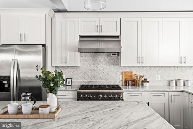 kitchen with range, light stone countertops, wall chimney range hood, stainless steel refrigerator with ice dispenser, and backsplash