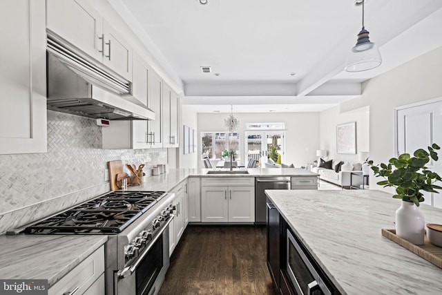 kitchen with under cabinet range hood, stainless steel appliances, a peninsula, a sink, and dark wood finished floors