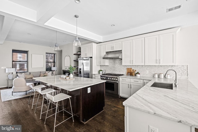 kitchen with visible vents, appliances with stainless steel finishes, a sink, under cabinet range hood, and a kitchen bar