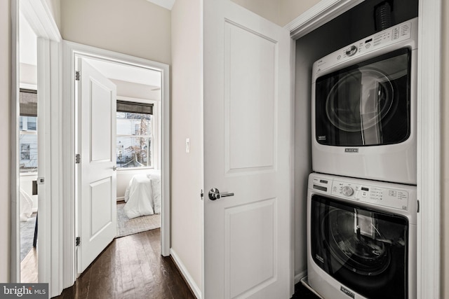 laundry area featuring baseboards, laundry area, dark wood-style flooring, and stacked washer / drying machine