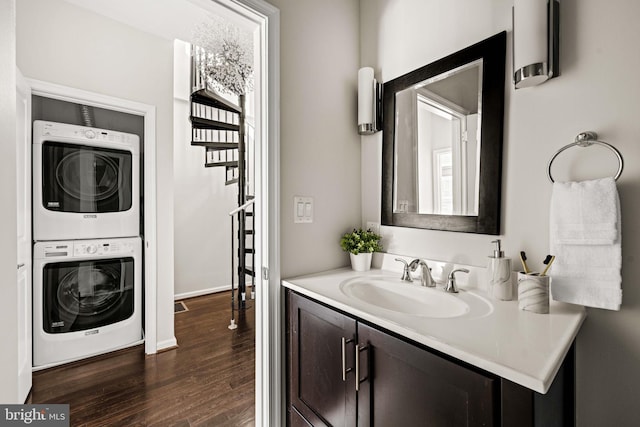 bathroom with stacked washer and dryer, vanity, baseboards, and wood finished floors