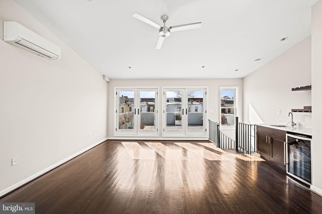 unfurnished living room with wine cooler, wood finished floors, a sink, baseboards, and a wall mounted AC