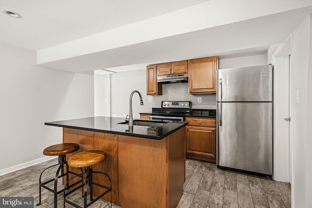 kitchen featuring stainless steel appliances, dark countertops, wood finish floors, and under cabinet range hood