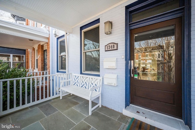 property entrance with a porch and brick siding