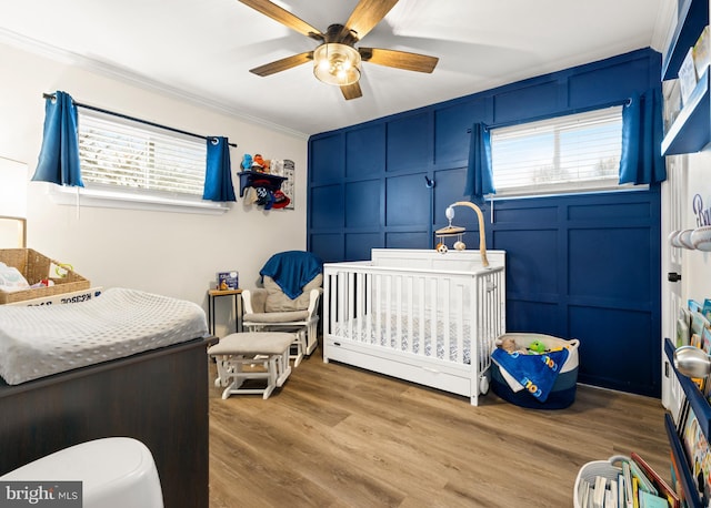 bedroom featuring crown molding, a decorative wall, a crib, and wood finished floors