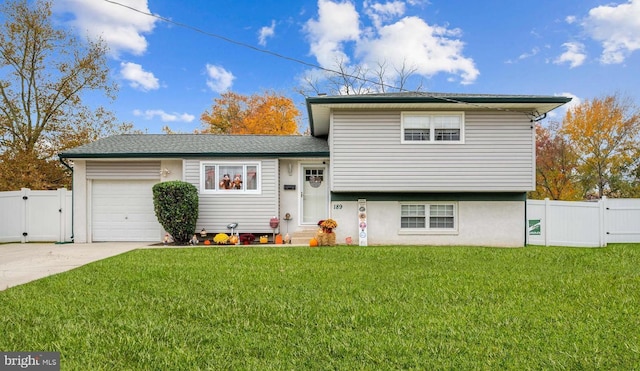 tri-level home with concrete driveway, an attached garage, a gate, fence, and a front lawn