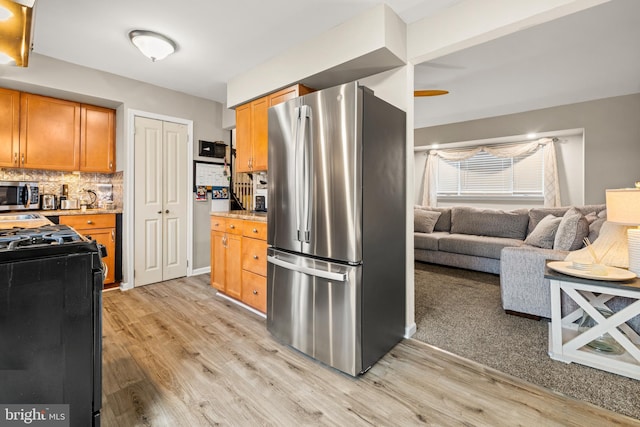 kitchen with brown cabinetry, appliances with stainless steel finishes, open floor plan, light wood-style floors, and backsplash