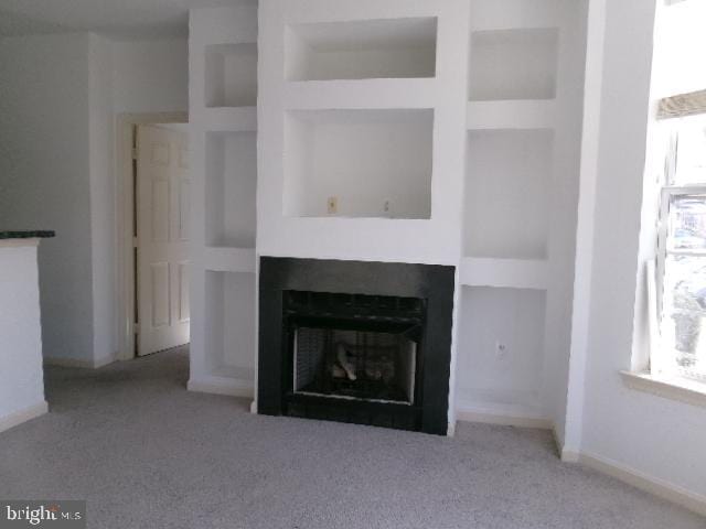 unfurnished living room featuring carpet floors, a fireplace, a wealth of natural light, and built in features