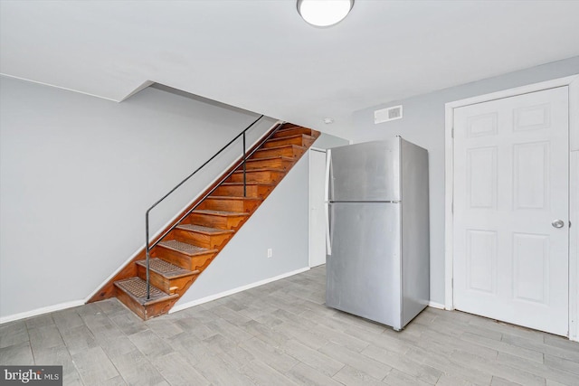 basement with baseboards, visible vents, freestanding refrigerator, stairs, and light wood-type flooring