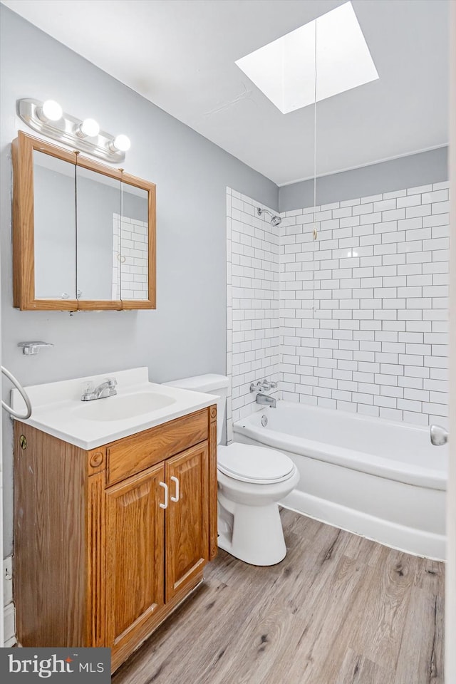 bathroom featuring a skylight, shower / bath combination, toilet, vanity, and wood finished floors