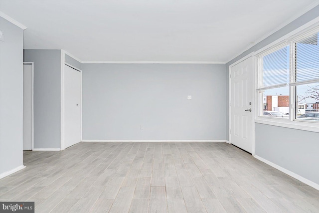 empty room featuring light wood-type flooring, crown molding, and baseboards