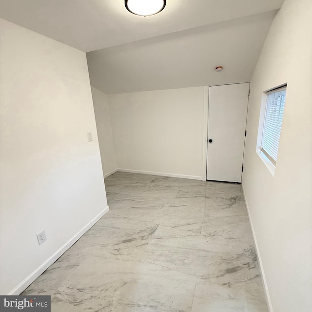 spare room with lofted ceiling, marble finish floor, and baseboards