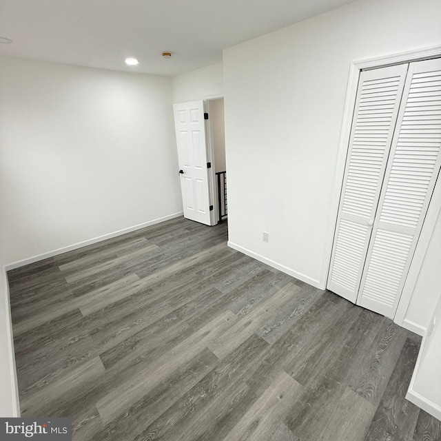 unfurnished bedroom with a closet, baseboards, and dark wood-type flooring