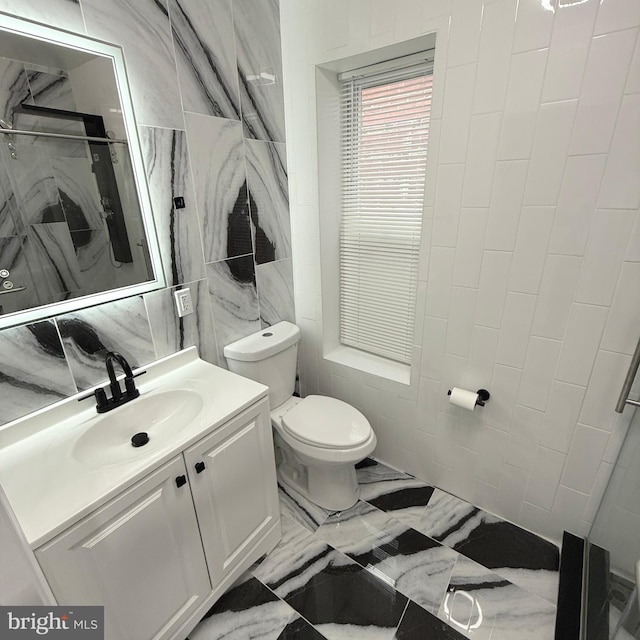 bathroom featuring toilet, vanity, tile walls, marble finish floor, and a shower stall