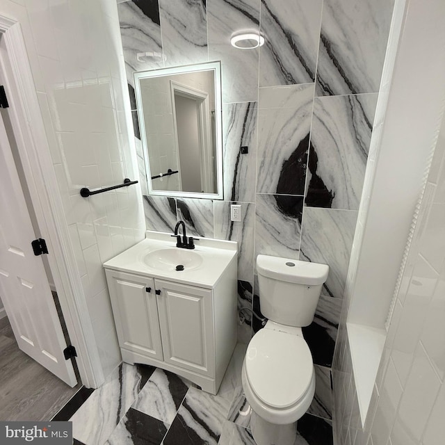 bathroom featuring toilet, marble finish floor, tile walls, and vanity