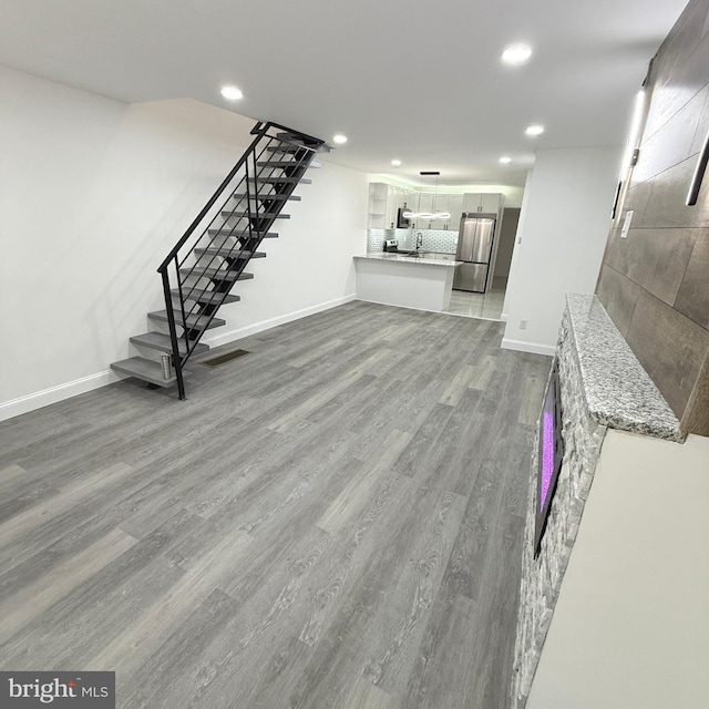 unfurnished living room featuring baseboards, stairway, wood finished floors, and recessed lighting