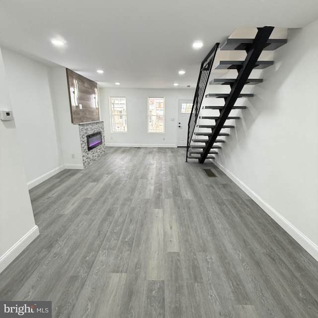 unfurnished living room featuring baseboards, a glass covered fireplace, dark wood-type flooring, stairs, and recessed lighting