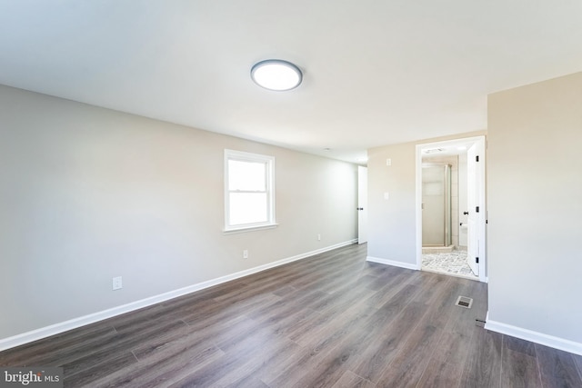 unfurnished room featuring dark wood finished floors, visible vents, and baseboards