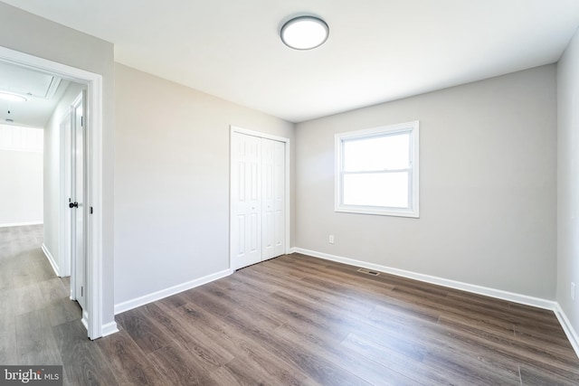 unfurnished bedroom featuring visible vents, dark wood-style floors, a closet, baseboards, and attic access