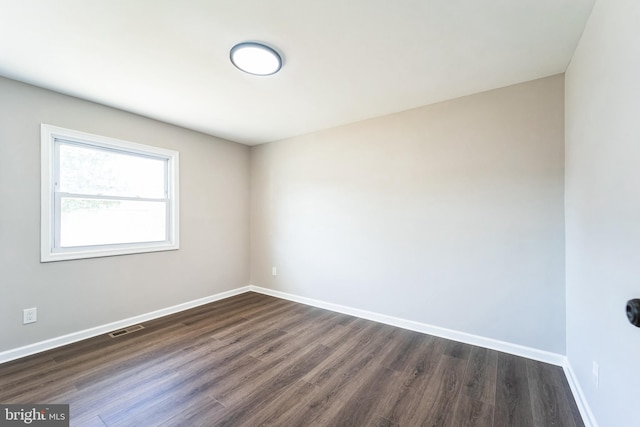 spare room with visible vents, baseboards, and dark wood finished floors