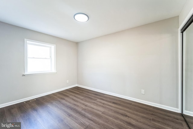 empty room featuring dark wood finished floors, visible vents, and baseboards