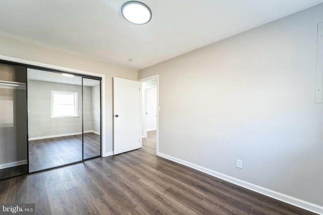 unfurnished bedroom with a closet, baseboards, and dark wood-style flooring