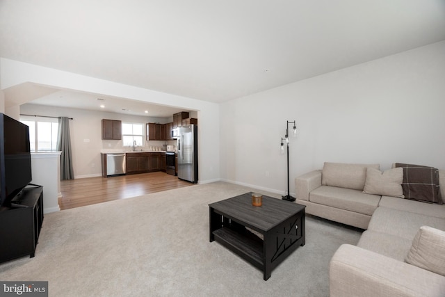living room with light colored carpet, recessed lighting, light wood-style flooring, and baseboards